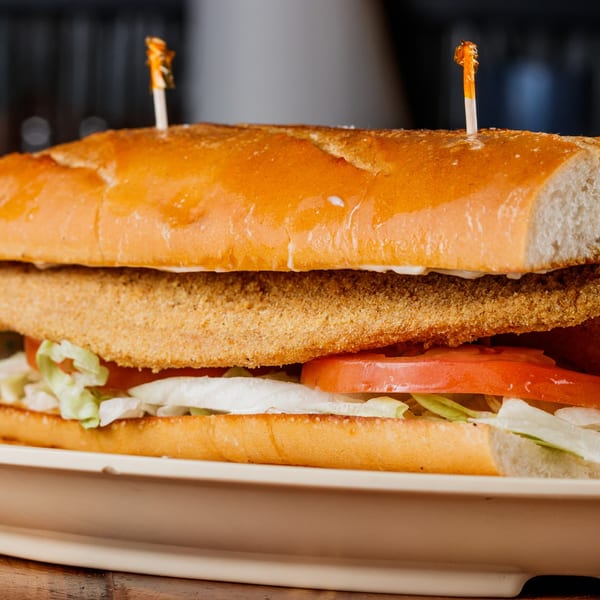 Golden fried fish po'boy on a toasted roll with lettuce and tomato.