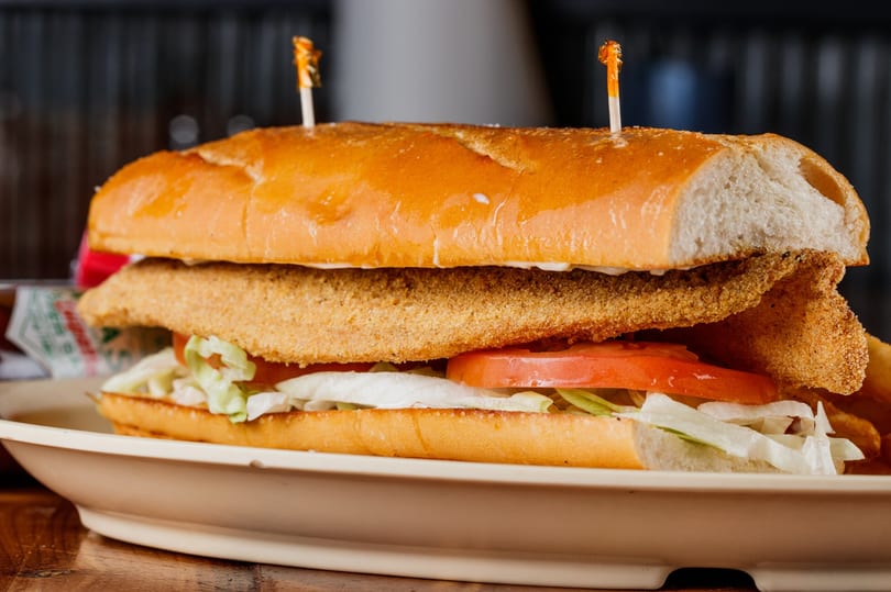 Golden fried fish po'boy on a toasted roll with lettuce and tomato.