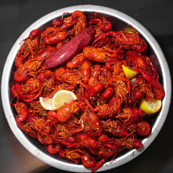 A metal bowl of seasoned crawfish boil with sausage and lemon.