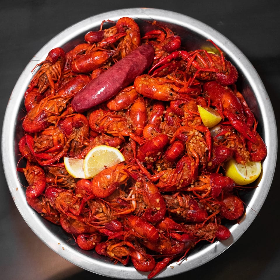 A metal bowl of seasoned crawfish boil with sausage and lemon.