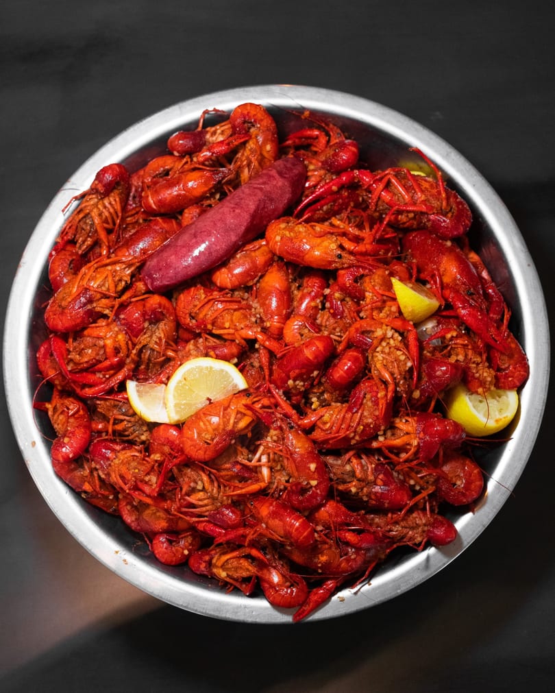 A metal bowl of seasoned crawfish boil with sausage and lemon.