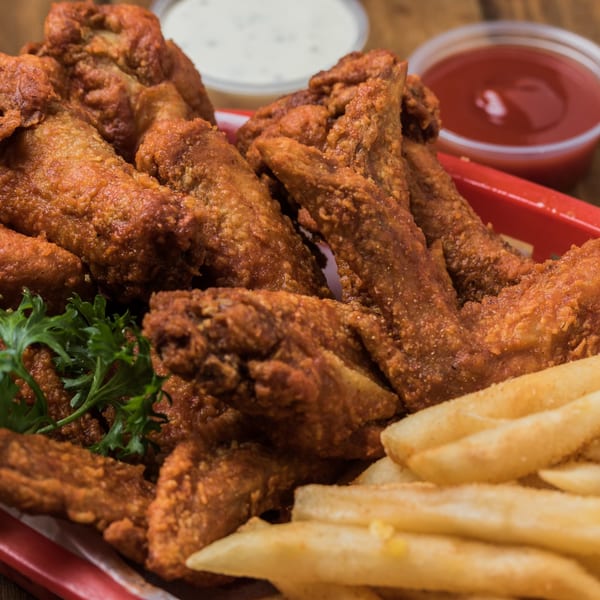 Crispy fried chicken wings with fries and dipping sauces on a red plate.