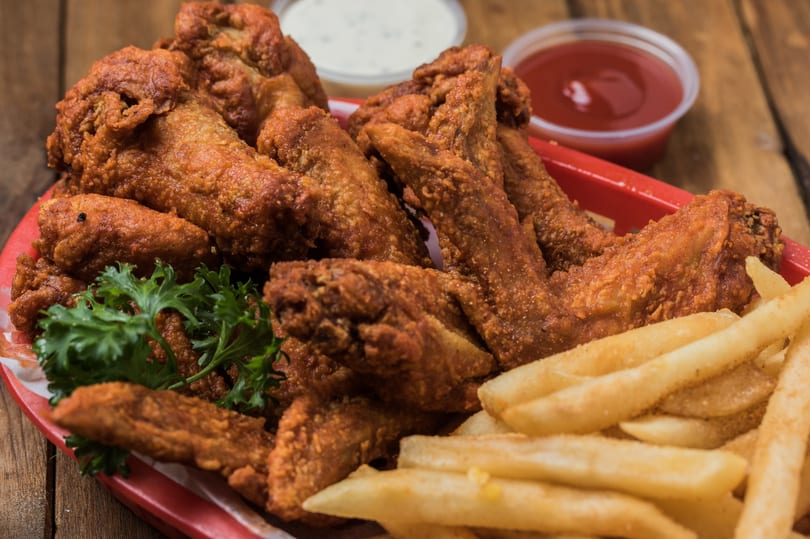 Crispy fried chicken wings with fries and dipping sauces on a red plate.