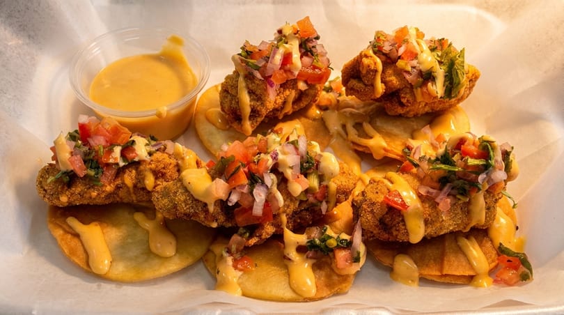 Fried green tomatoes topped with pico de gallo and a creamy sauce, served with a side of dipping sauce.